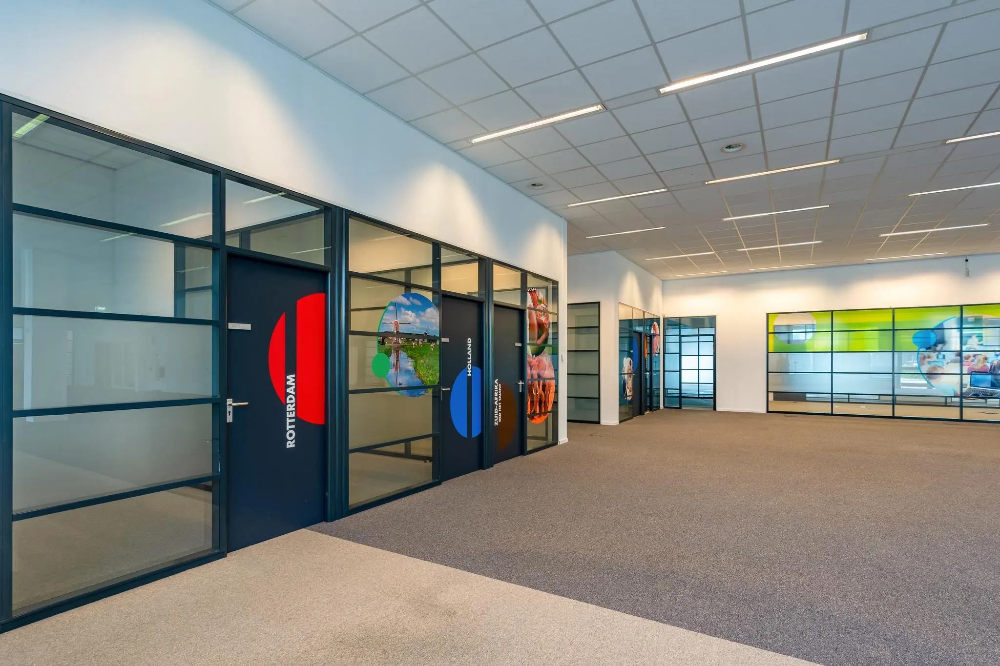 Moderne kantoorruimte aan de Rivium Boulevard met glazen wanden en deuren voorzien van kleurrijke afbeeldingen en stadsnamen.